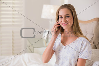 Natural cheerful woman sitting in bed phoning