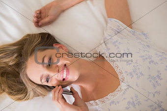 Natural happy woman lying on bed phoning