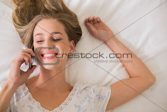 Natural smiling woman lying on bed phoning