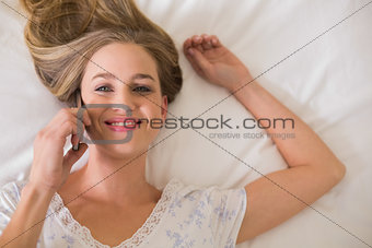 Natural cheerful woman lying on bed phoning