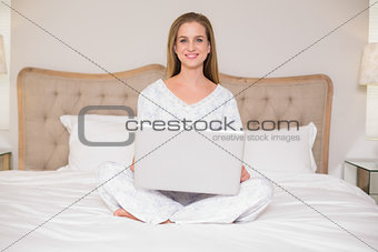 Natural happy woman sitting on bed using laptop