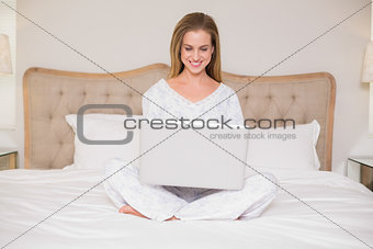 Natural smiling woman sitting on bed using laptop