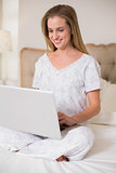Natural content woman sitting on bed using laptop