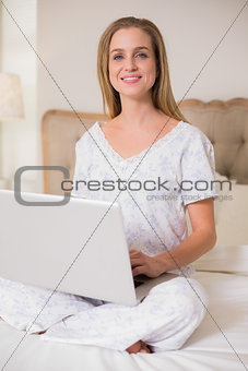 Natural cheerful woman sitting on bed using laptop