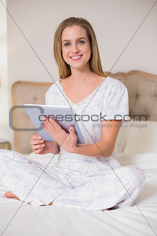 Natural cheerful woman sitting on bed using tablet