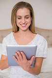Natural content woman sitting on bed using tablet