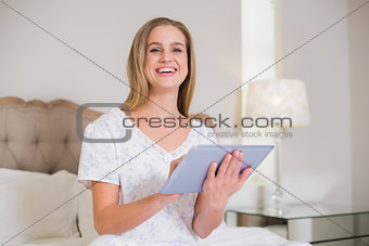 Natural laughing woman sitting on bed holding tablet