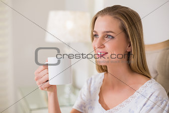 Natural happy woman sitting on bed holding mug