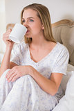 Natural calm woman sitting on bed drinking