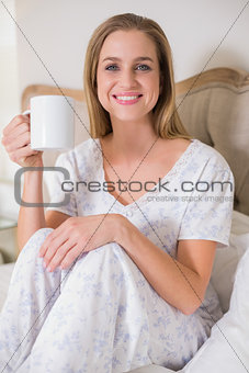 Natural smiling woman sitting on bed holding mug