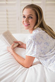 Natural happy woman lying on bed holding book