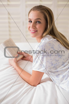 Natural happy woman lying on bed holding book