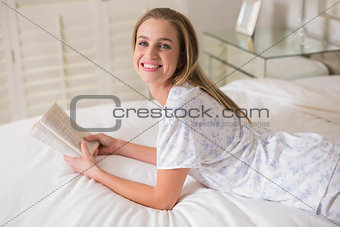 Natural smiling woman lying on bed holding book