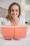 Natural smiling woman lying on bed reading
