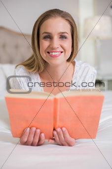 Natural cheerful woman lying on bed holding book