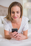 Natural content woman lying on bed holding smartphone