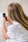 Natural woman lying on bed using smartphone