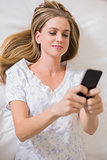 Natural calm woman lying on bed using smartphone