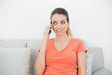 Thinking young woman phoning with her smartphone sitting on couch