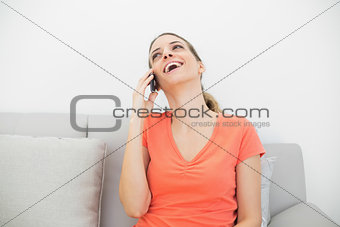 Laughing casual woman phoning with her smartphone sitting on couch