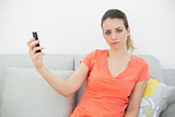 Serious cute woman holding her smartphone sitting on couch