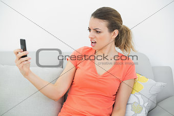 Shocked woman looking at her smartphone sitting on couch