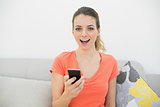 Happy casual woman holding her smartphone sitting on couch