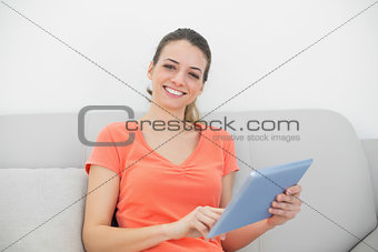 Cheerfully smiling woman working with her tablet sitting on couch