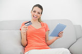 Attractive amused woman home shopping with her tablet smiling at camera