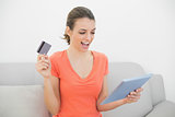 Cheerful casual woman home shopping with her tablet sitting on couch