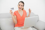 Beautiful cheering woman presenting her credit card sitting on couch