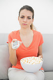 Irritated young woman watching television sitting on couch