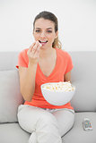 Amused young woman watching television eating popcorn