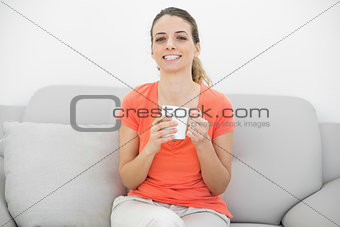 Cheerful beautiful woman holding a cup sitting on couch