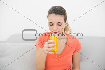 Lovely woman drinking a glass of orange juice sitting on couch