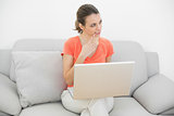 Attractive thoughtful woman using her notebook sitting on couch