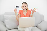 Happy casual woman showing her credit card using her notebook