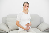 Young pregnant woman posing sitting on couch smiling at camera