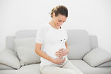 Proud pregnant woman sitting on couch touching her belly