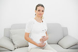 Beautiful calm pregnant woman holding her belly sitting on couch