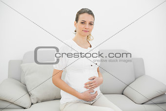 Beautiful calm pregnant woman holding her belly sitting on couch