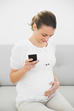 Beautiful pregnant woman holding her smartphone holding happily her belly