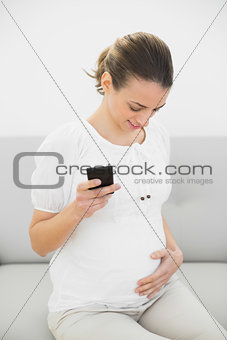 Beautiful pregnant woman holding her smartphone holding happily her belly