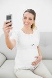 Attractive smiling pregnant woman taking a self-portrait with her smartphone