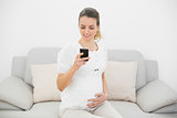 Pretty pregnant woman using her smartphone touching her belly