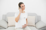 Smiling pregnant woman phoning with her smartphone sitting on couch