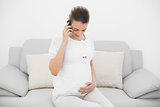 Young pregnant woman phoning while holding her belly and looking at it