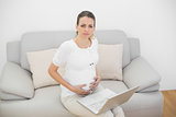 Serious pregnant woman holding her belly sitting on couch