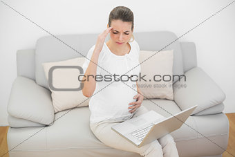 Pregnant woman having headache touching her belly sitting on couch