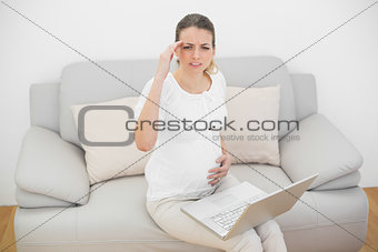 Young pregnant woman sitting on couch looking suffering at camera